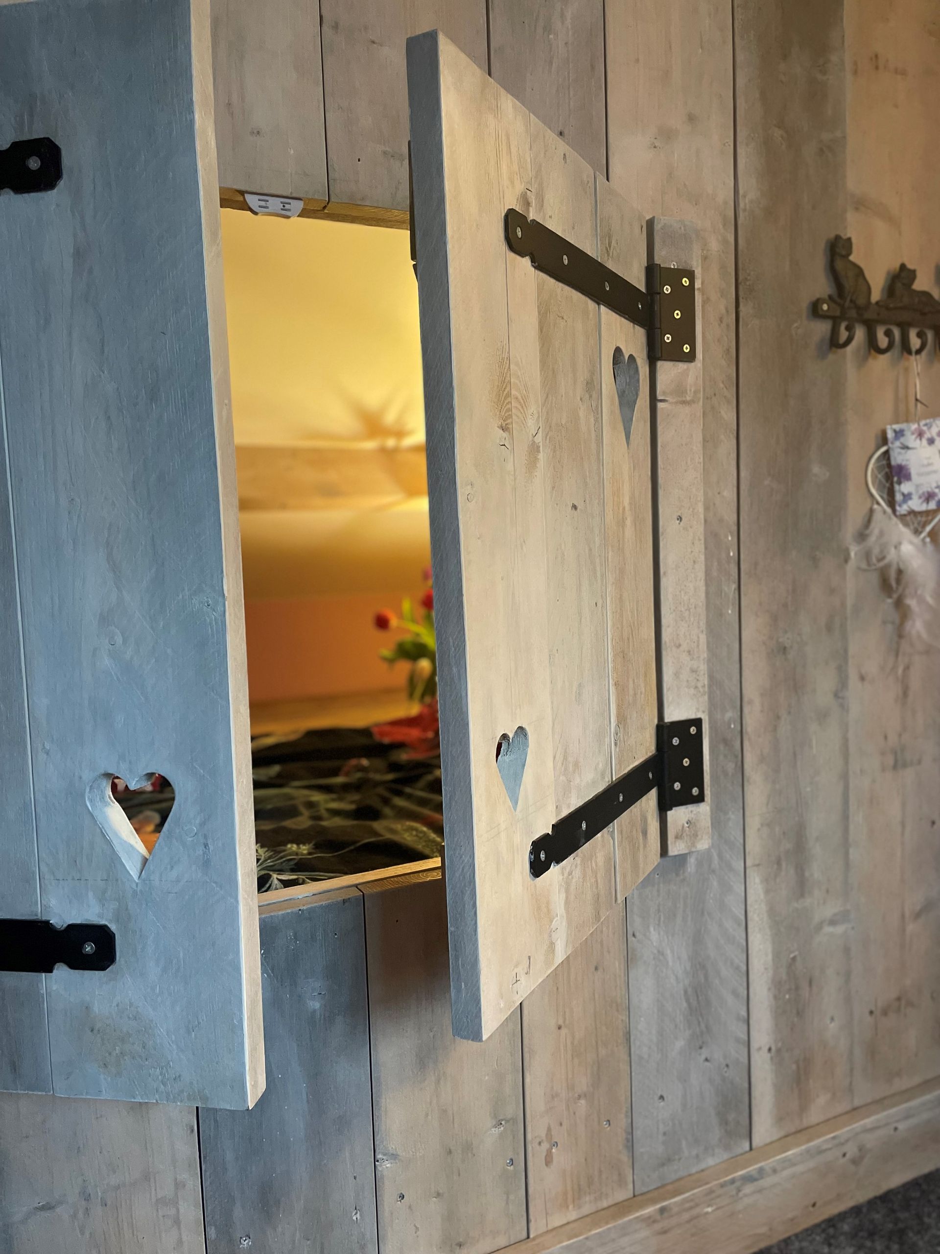 Rustieke houten luiken openen zich en onthullen een tafereel met geel/oranje licht. De muur is gemaakt van houten planken.