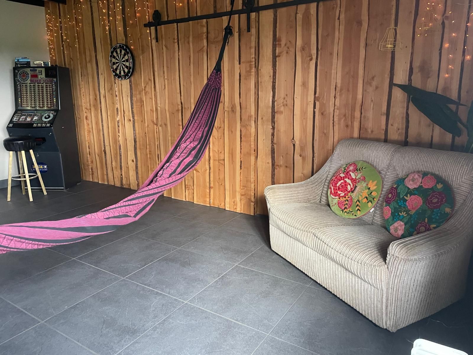 Gezellige kamer met een houten lambrisering. Er staan ​​een bank met bloemenkussens, een hangmat en een arcadekast.