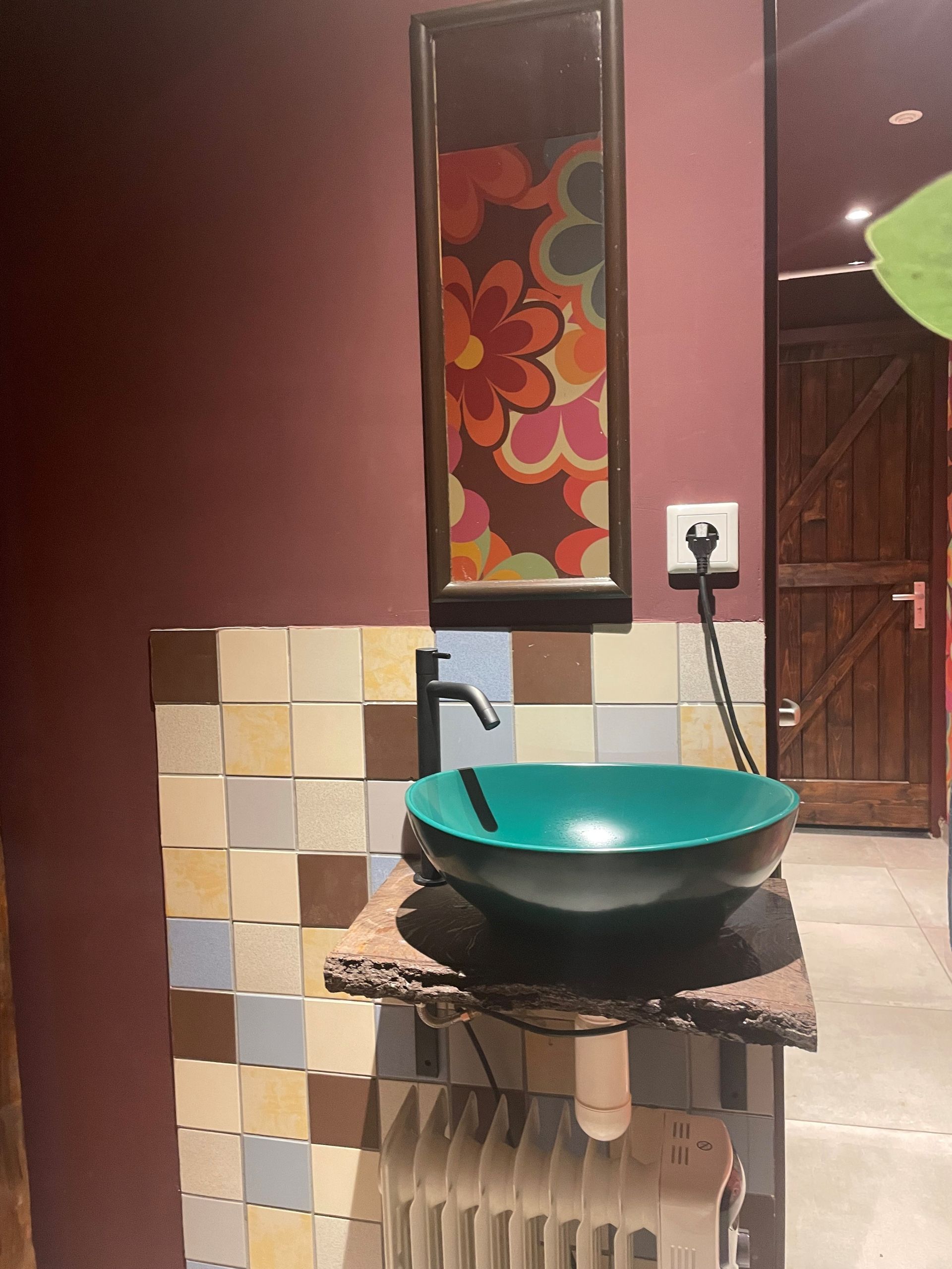 Een kleine wastafel in de badkamer met een turquoise kom op een houten blad, bloemmotieven en een betegelde muur.