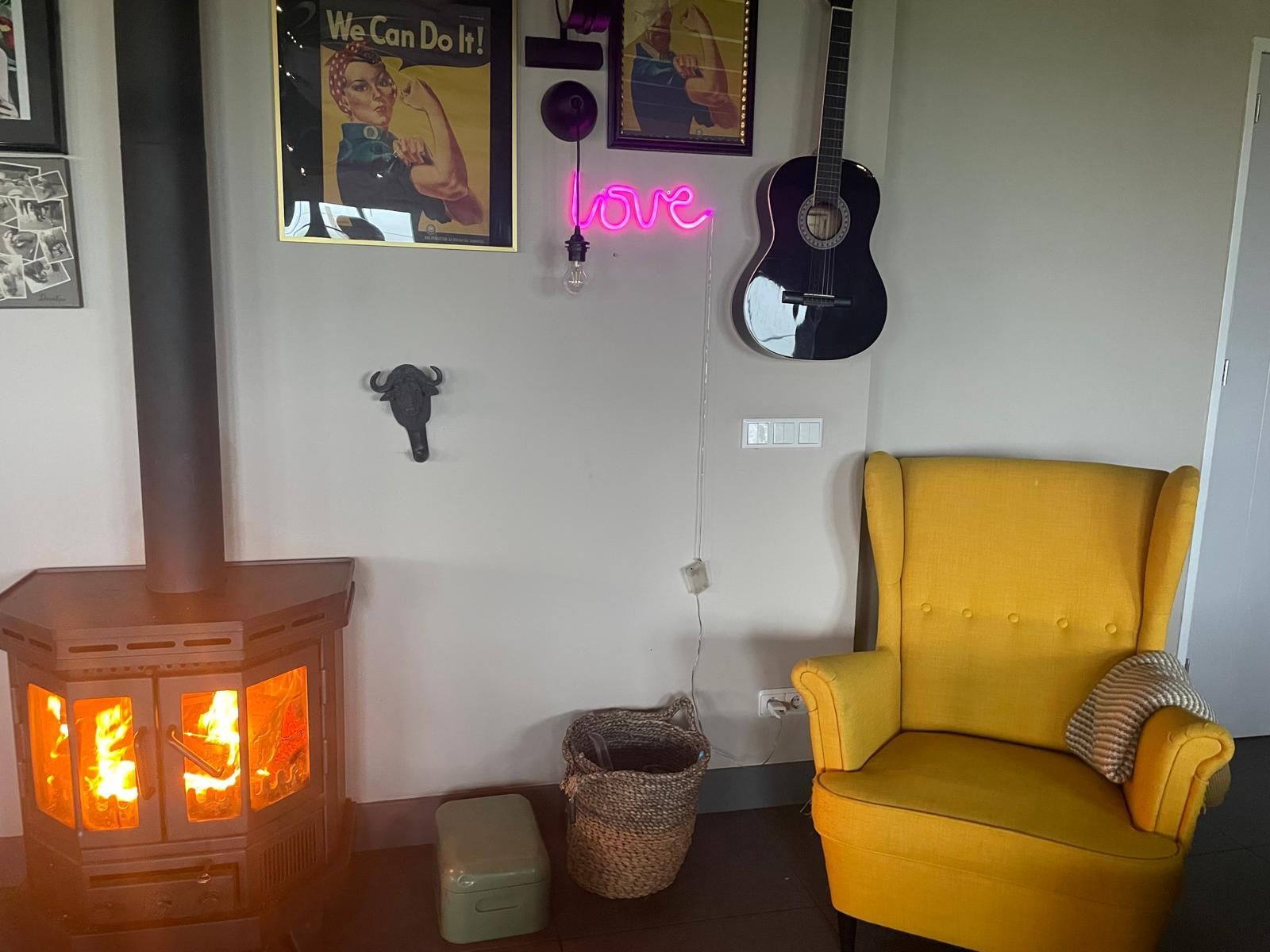 Gezellige kamer met brandende open haard, gele fauteuil, gitaar en een neonbord met het woord 