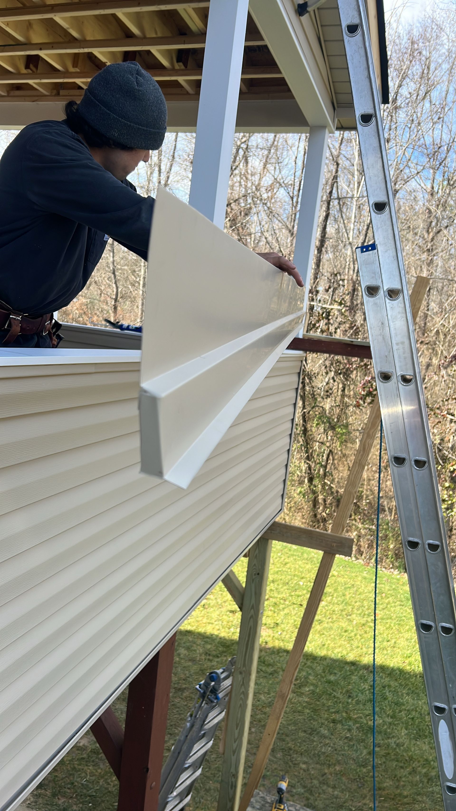 A man is standing on a ladder holding a piece of siding.