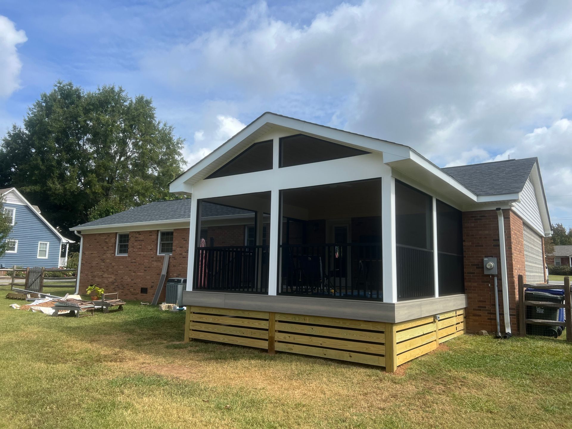 A screened in porch is being built on the side of a brick house.