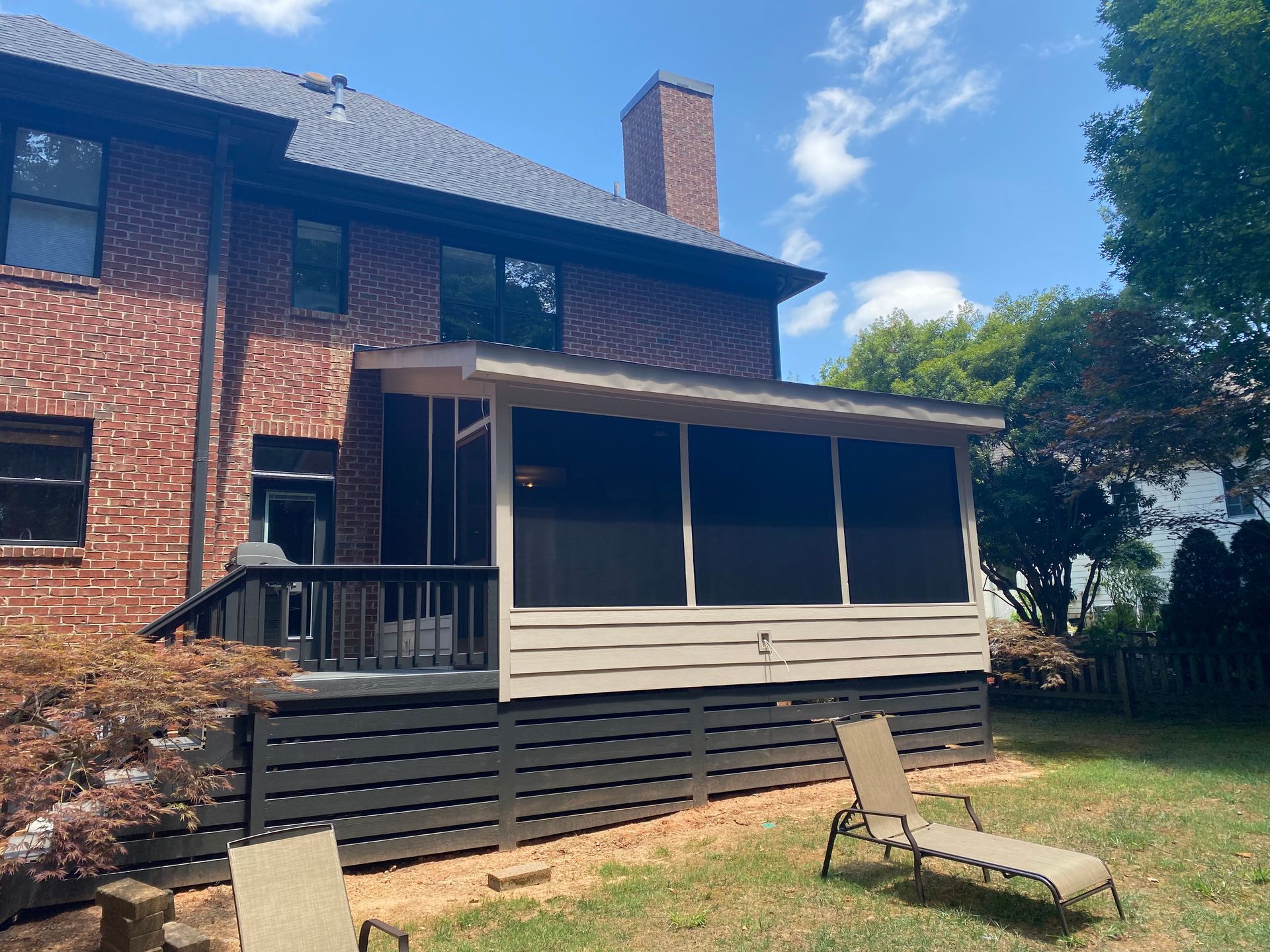A screened in porch with lawn chairs in front of a brick house.