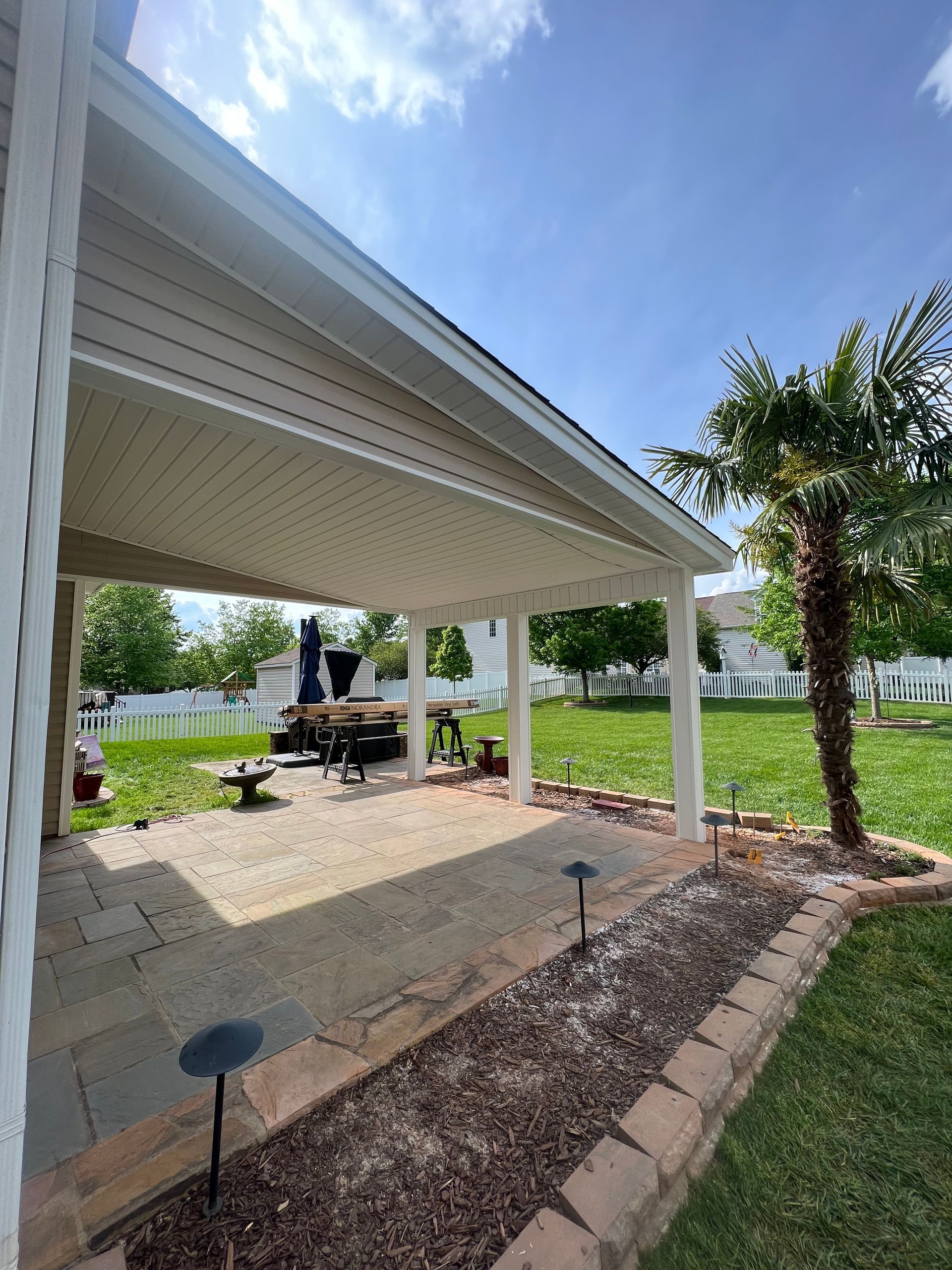 A patio with a covered area and a palm tree in the backyard.