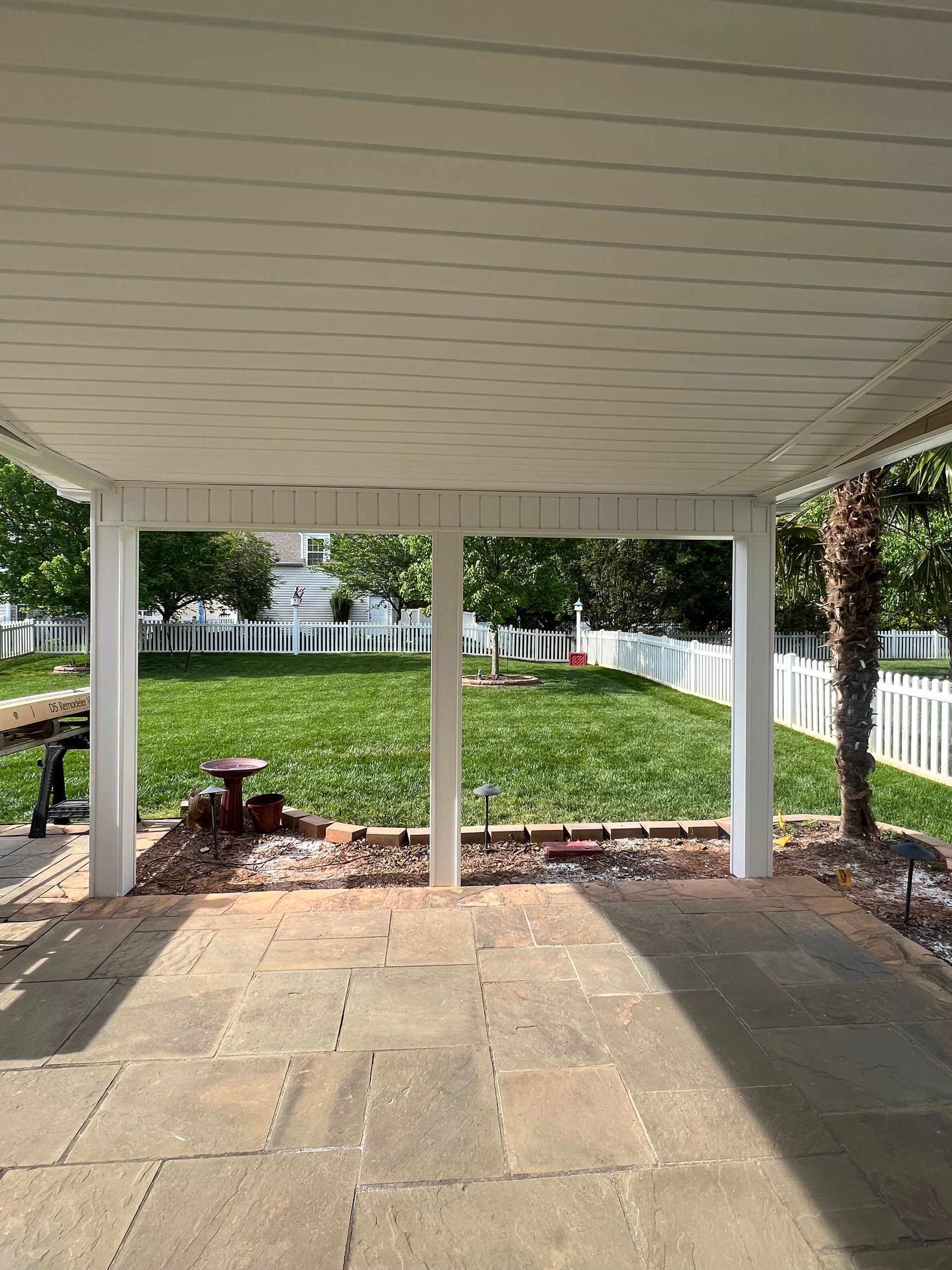 A covered patio with a view of a lush green yard.