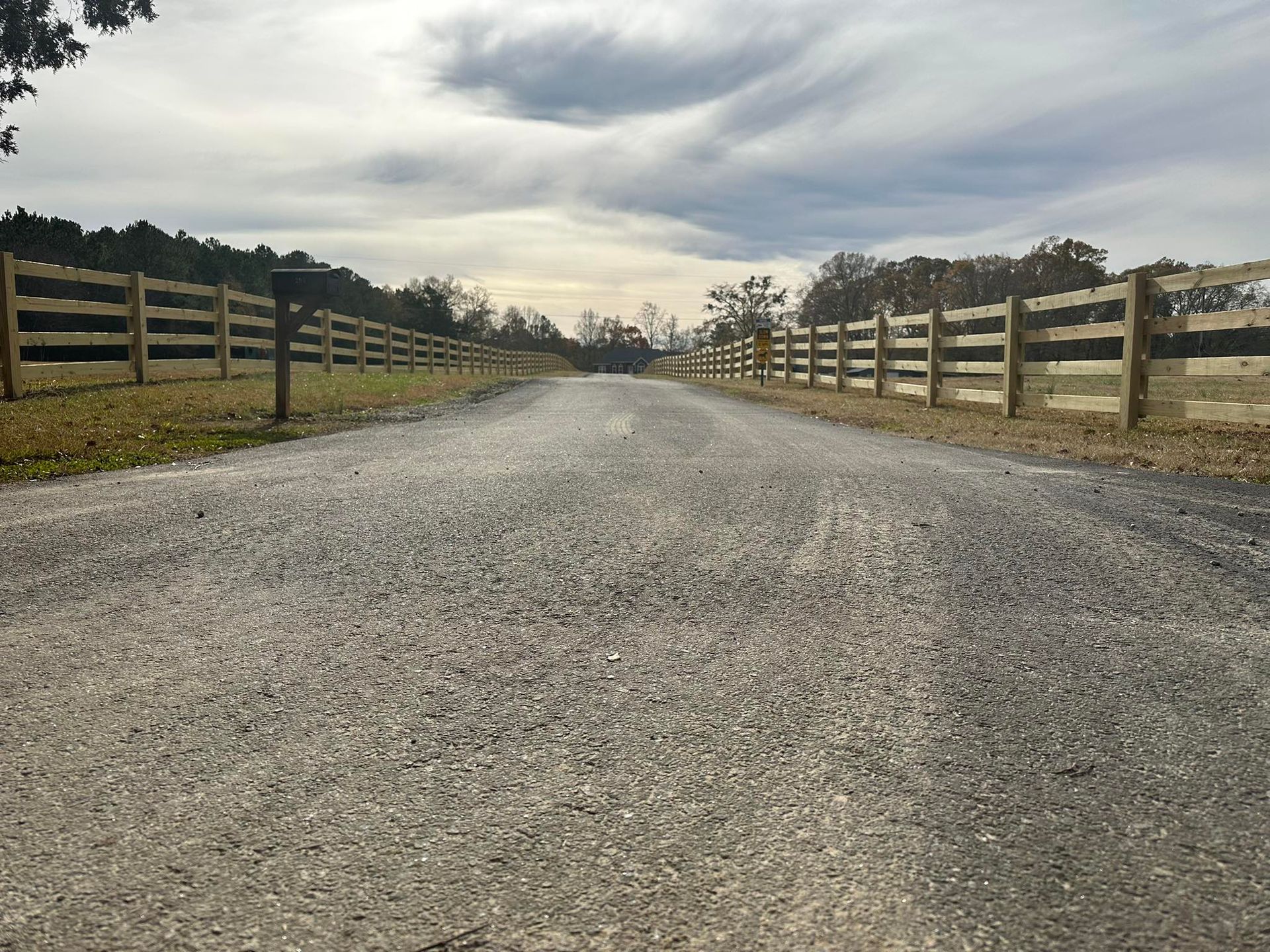 Gravel road flanked by wooden fences under a cloudy sky.