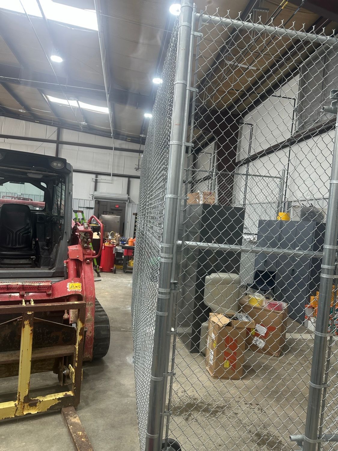 Chain-link fence inside a warehouse. A forklift and person are visible nearby.