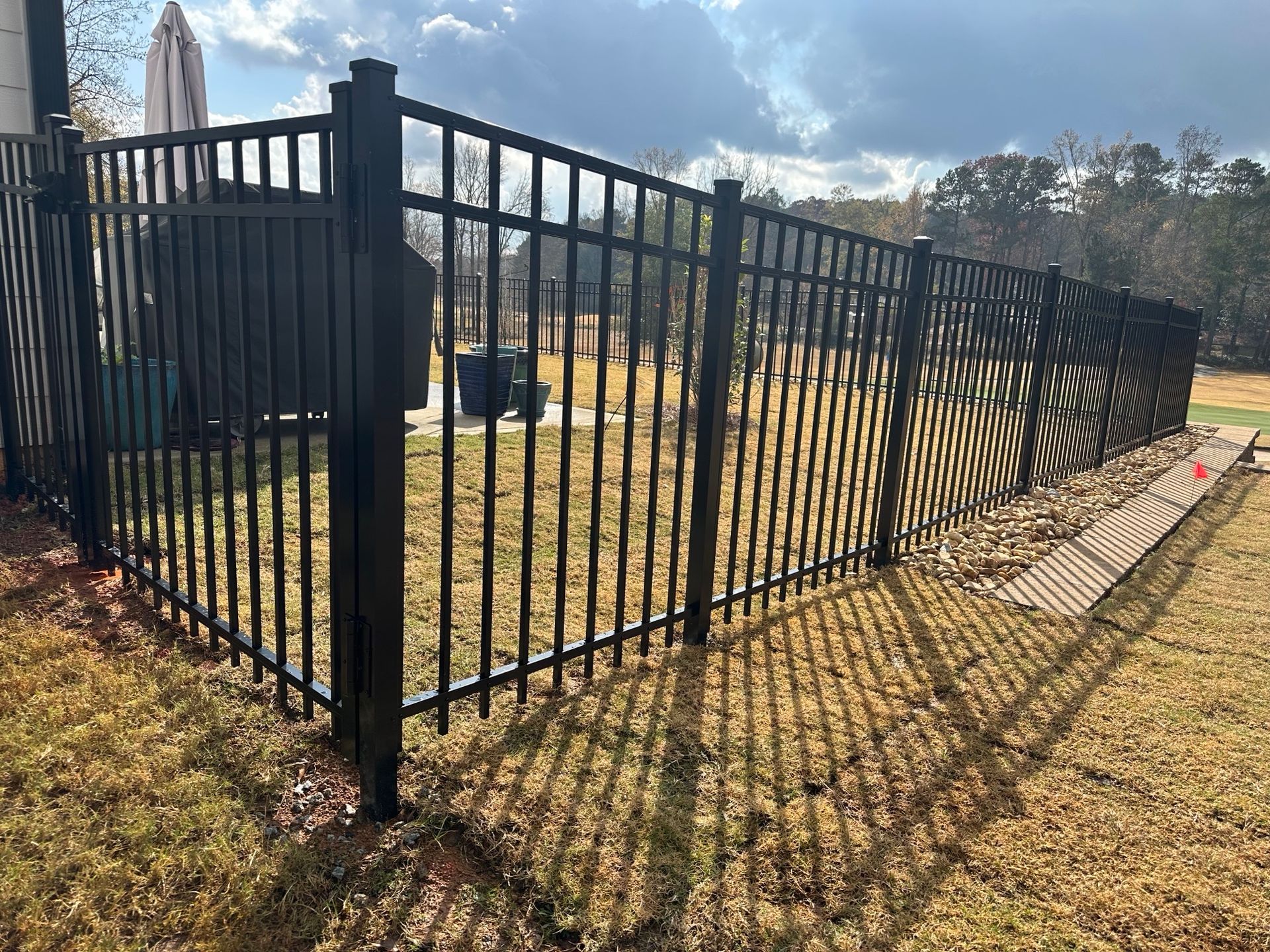 Black metal fence on grassy lawn with sunlit shadows.