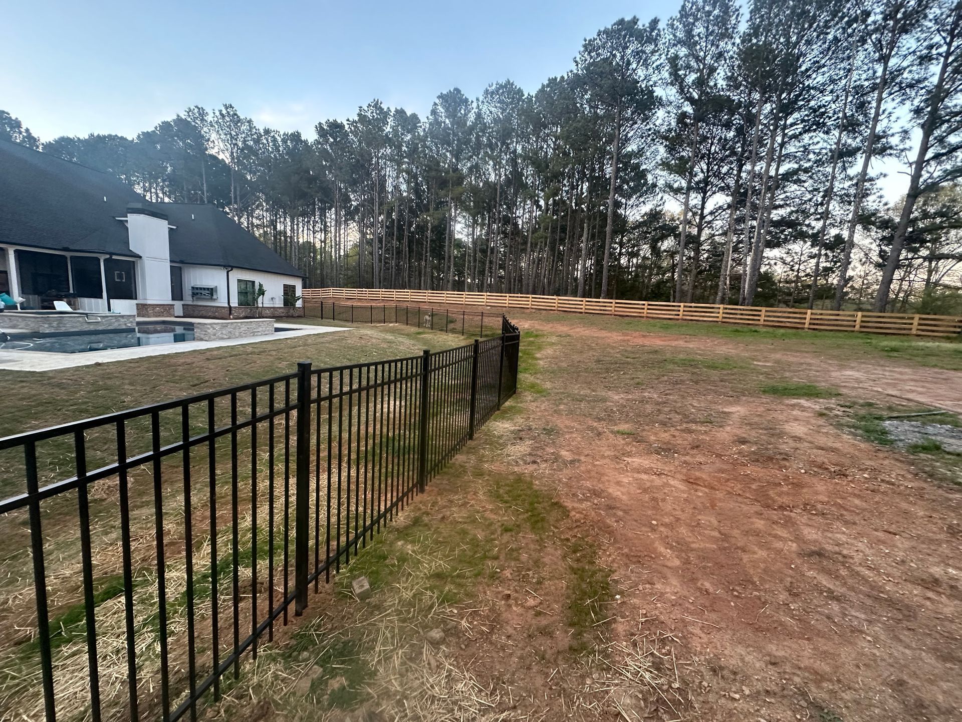 Black fence in a grassy yard, house in the background, trees along the horizon.