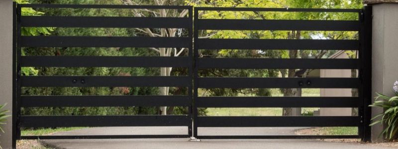 Black horizontal slat gate, open, with greenery visible in background.