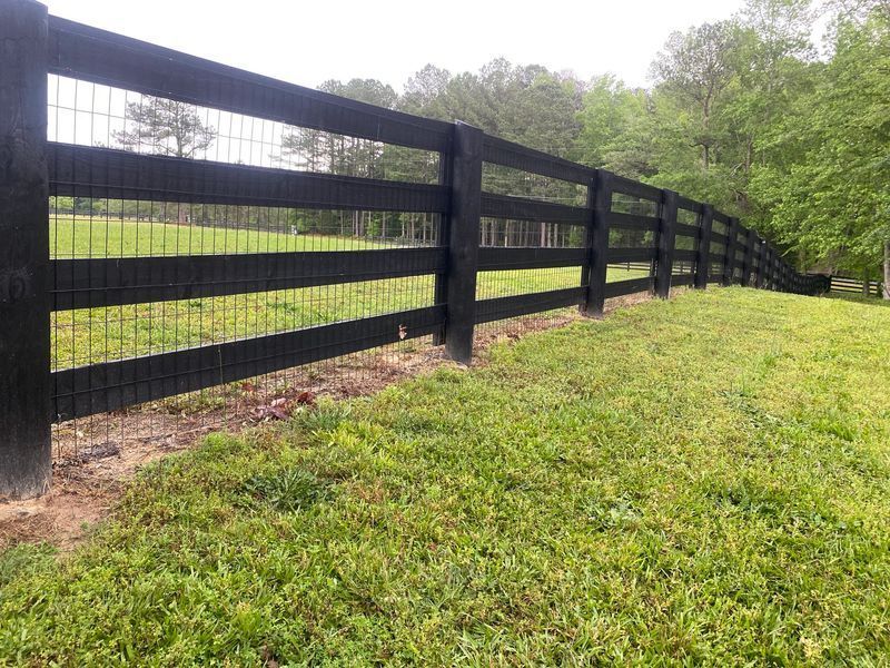 Black wooden fence with wire mesh in a grassy field.