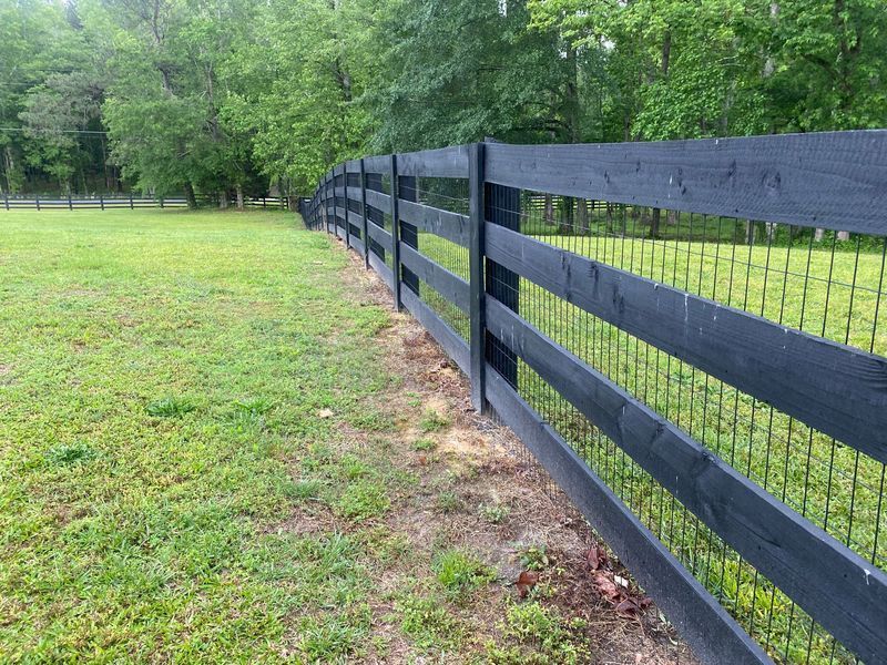 Black wooden fence enclosing a grassy field, with trees in the background.