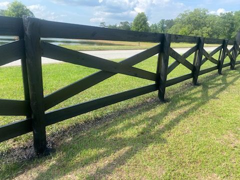 Black wooden fence in a grassy field, under a partly cloudy sky.