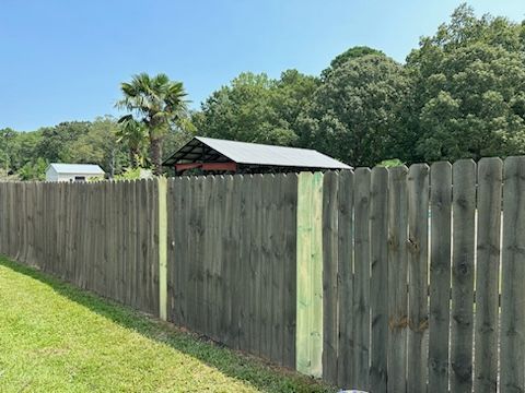 Wooden fence in a yard with a shed and trees in the background. Bright sunny day.