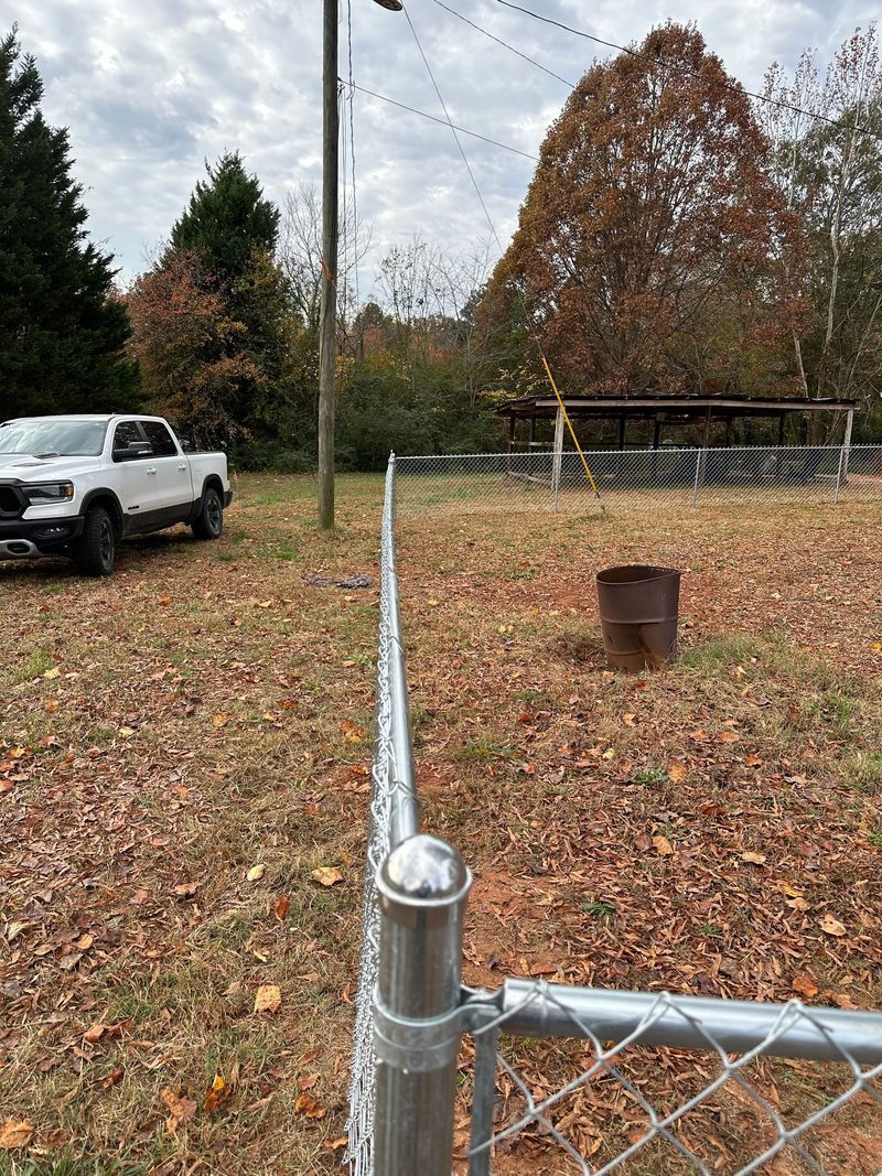 A chain-link fence lines a yard with a white truck parked near trees under a cloudy sky.