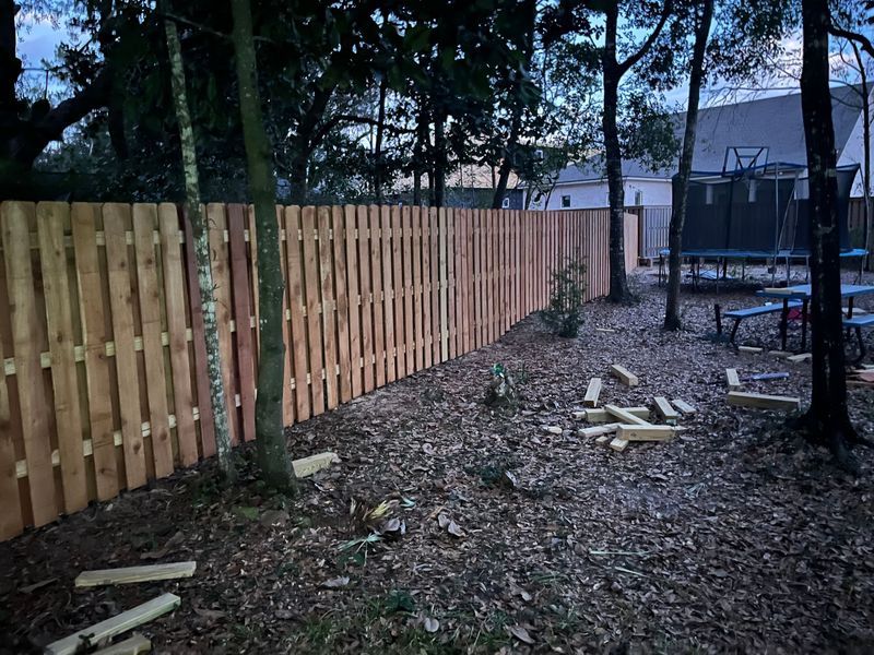 Wooden privacy fence in a backyard setting, with a trampoline and benches visible.