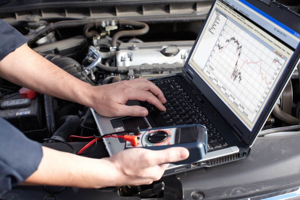 Laptop displaying car service diagnostics on a car engine. Hand on the diagnostic tool and computer doing a car service in canberra
