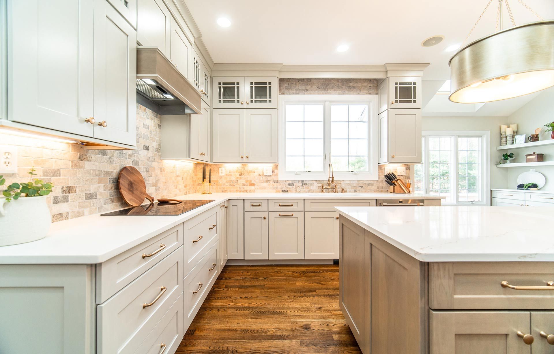 Bright modern white kitchen with large island, wood floors, and window over the sink