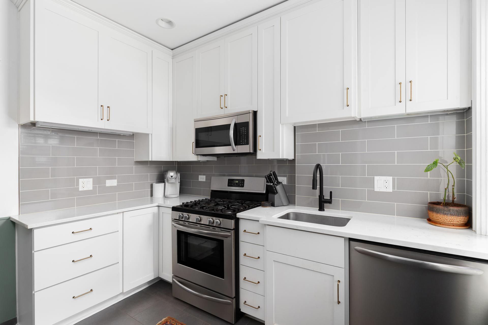 Bright white kitchen with gray tile backsplash, stainless steel appliances, and dark sink.