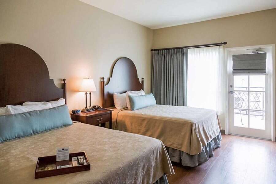 Hotel room with two twin beds, nightstand with lamp, and balcony door.