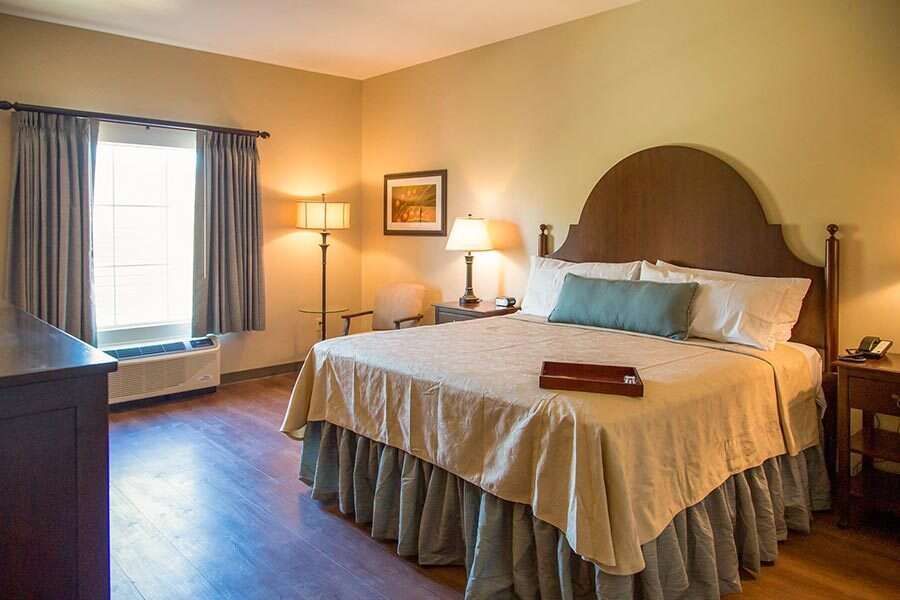 Bedroom with a bed, window, lamps, and furniture in warm tones.