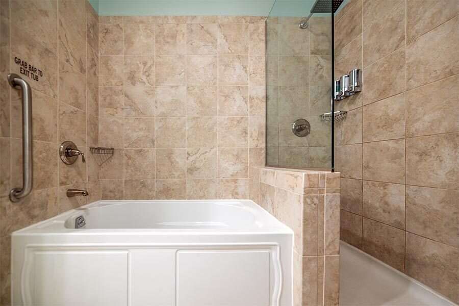 Bathroom with a low-entry tub and glass shower door, featuring grab bars and beige tile.