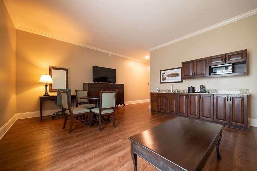 Spacious hotel suite with table and chairs, desk with mirror, and kitchenette with cabinets.
