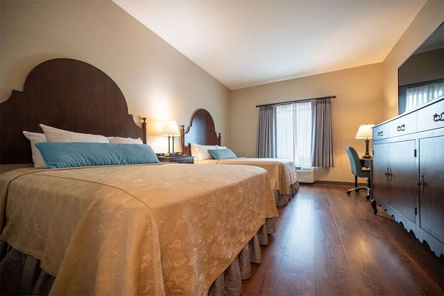 Hotel room with two beds, brown headboards, desk, and television.
