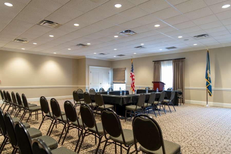 A meeting room with chairs facing a table draped in black, with an American flag and lectern.