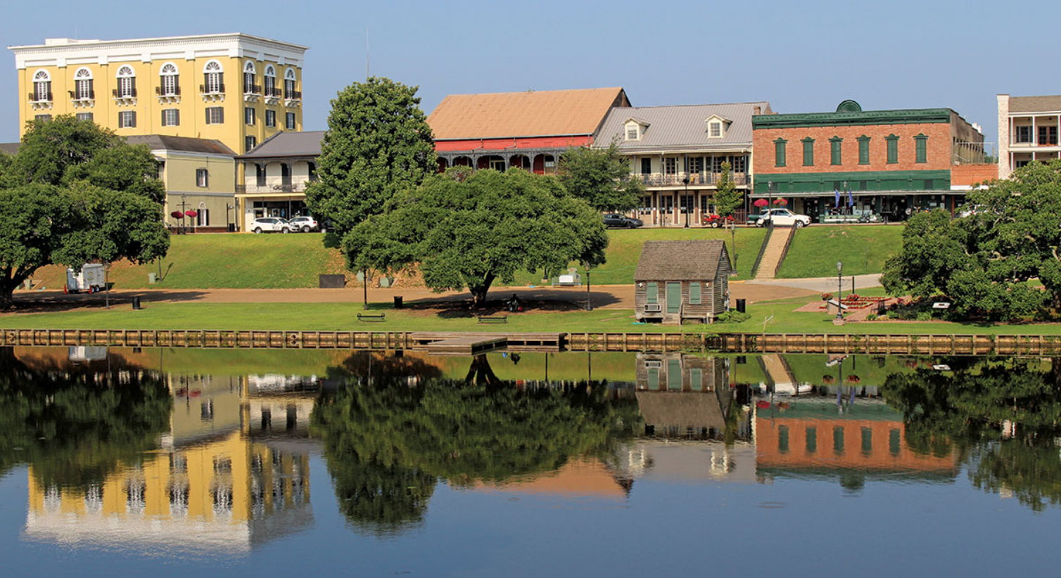 Hotel room with a bed, couch, dresser, and lamps. Wood floors and tan walls.