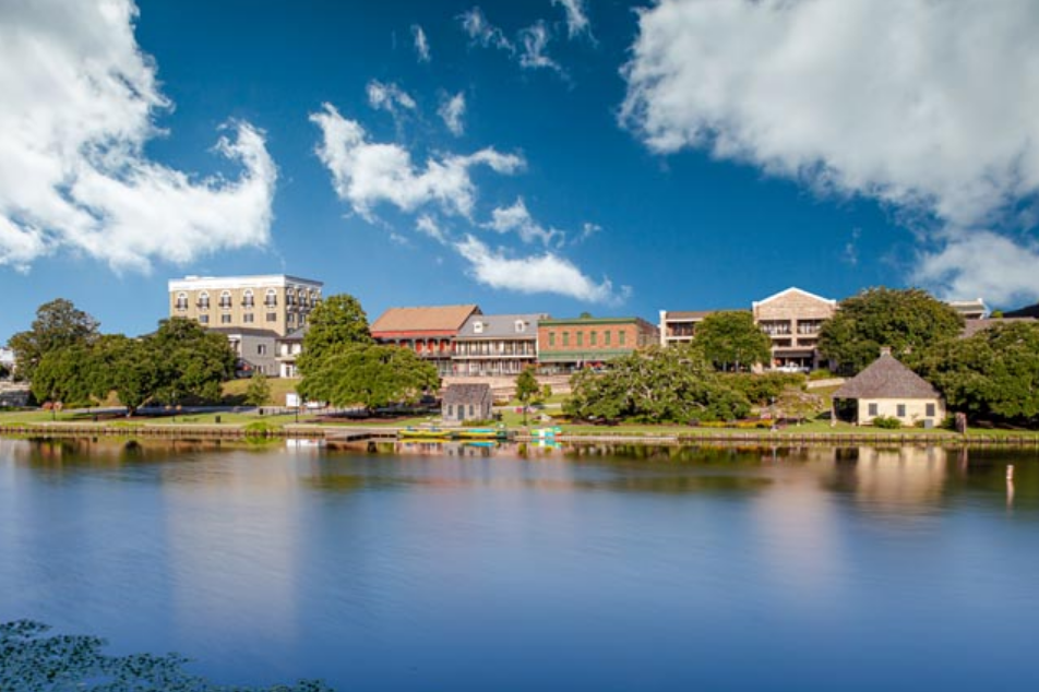 Living room with a sofa, coffee table, dining set, and window with curtains. Beige walls, hardwood floors.