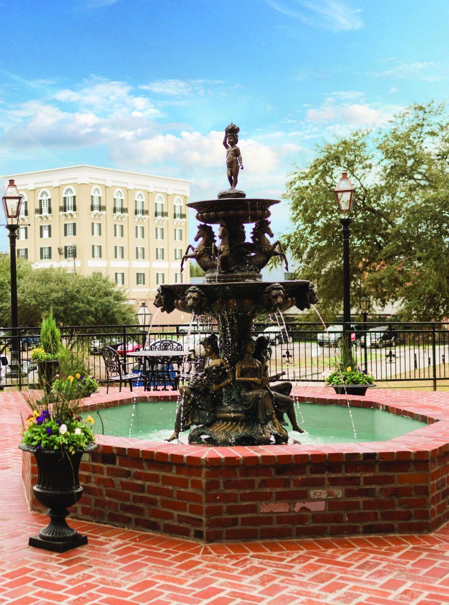 Fountain in a brick plaza with a building and trees in the background.