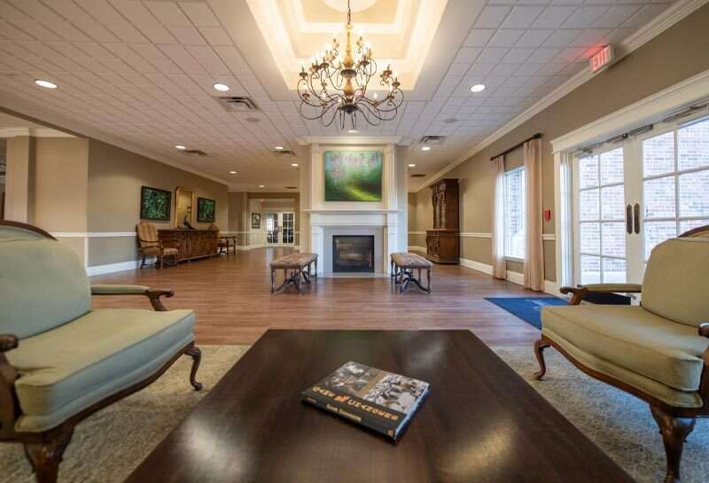 Lounge area with fireplace, armchairs, and chandelier. Wooden floor, artwork on walls.