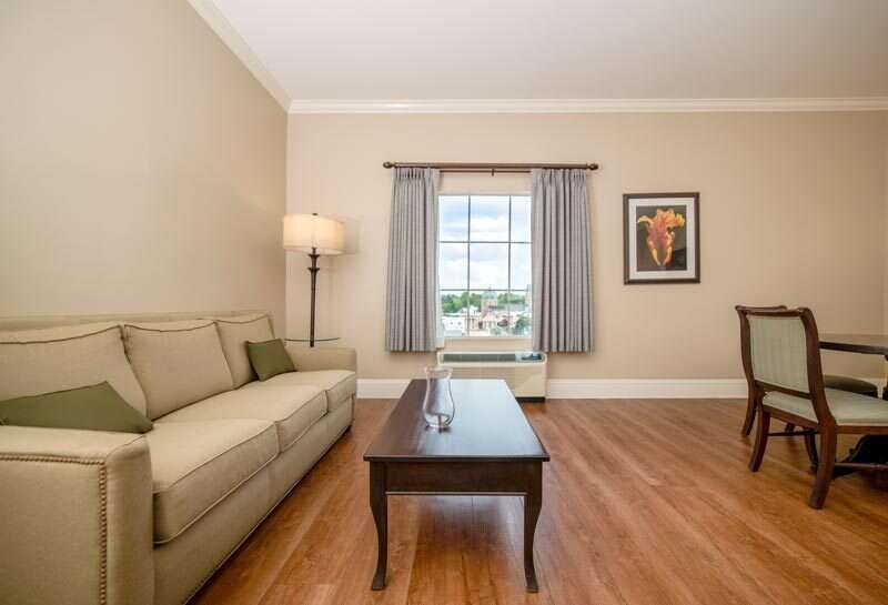 Living room with a sofa, coffee table, dining set, and window with curtains. Beige walls, hardwood floors.