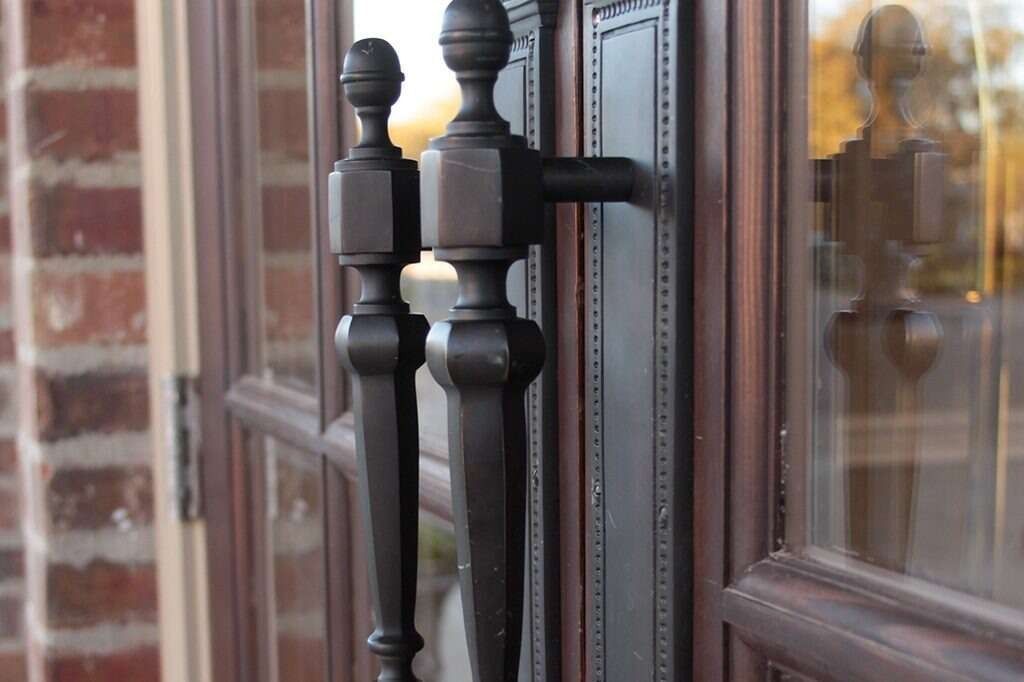 Black door handle on a brown glass door, with brick wall in the background.