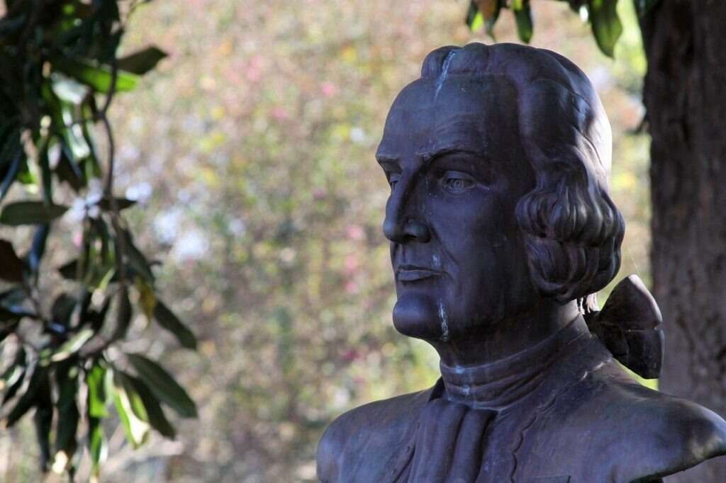 Bronze bust of Christopher Columbus with blurred foliage in the background.