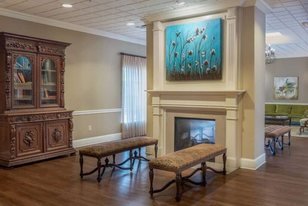 Lobby with fireplace, ornate cabinet, benches. Turquoise artwork above fireplace, light walls, and wood floors.