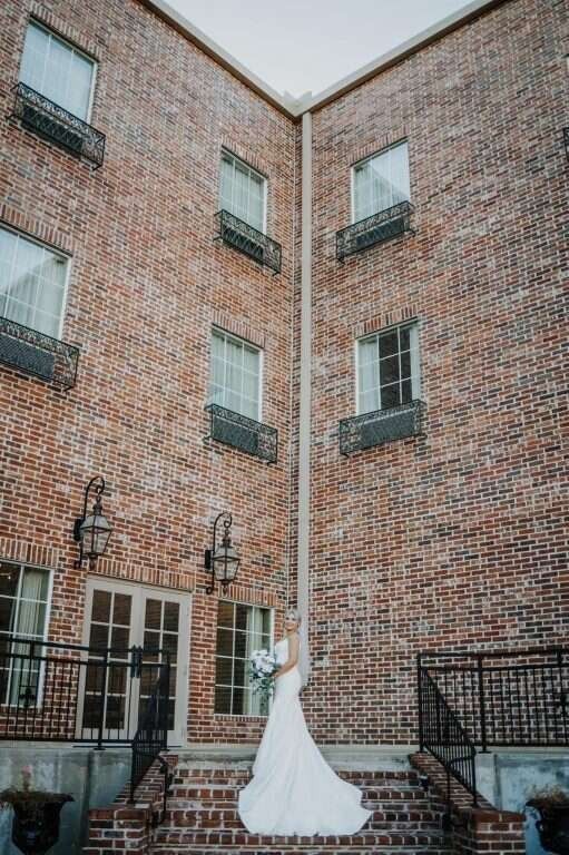 Woman in a white wedding dress stands on brick steps in front of a brick building.