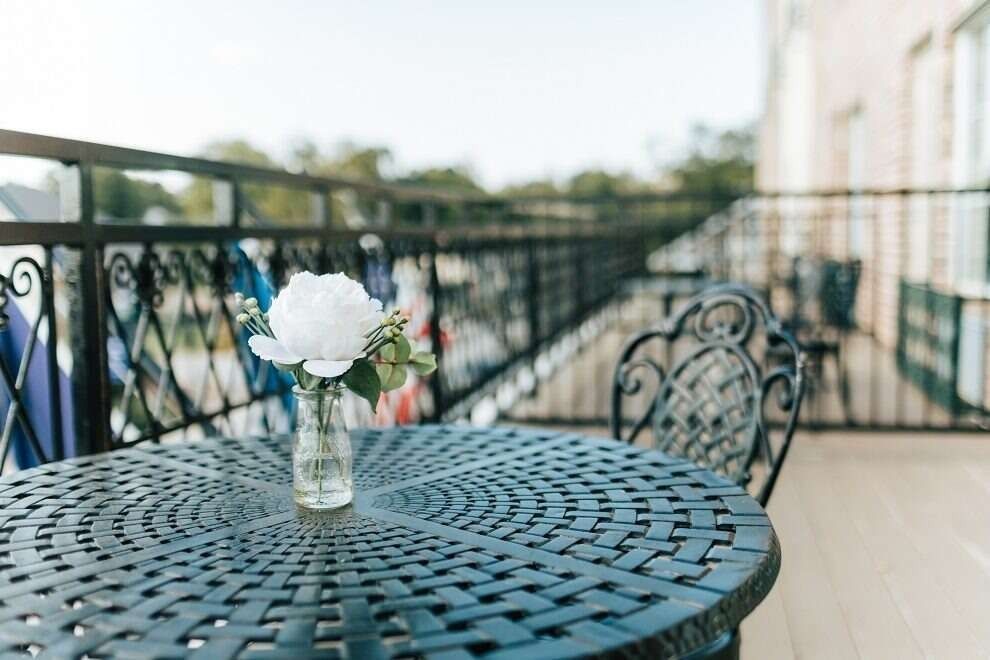 A small table on a balcony with a vase of white flowers and a wrought iron railing.