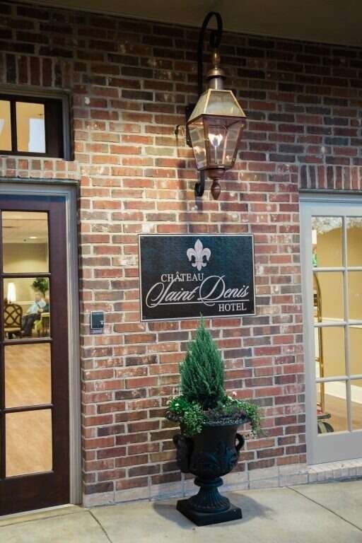 Entrance to the Château Saint Denis Hotel: brick building, dark sign, lantern, and decorative potted plant.