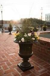 Black urn planter with white flowers and greenery on a brick patio at dusk.