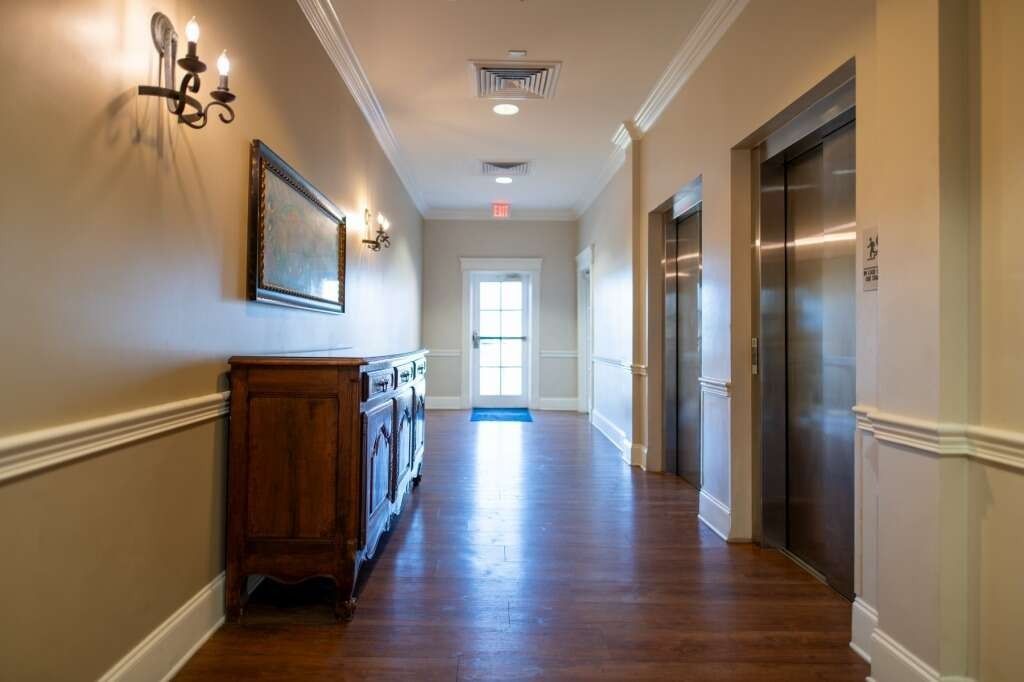Hallway with wooden floors, elevators, and a decorative cabinet.