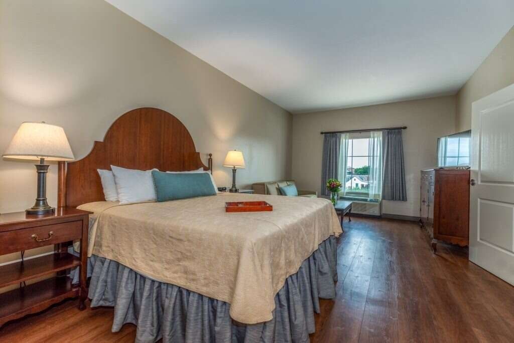 Hotel room with king bed, nightstand, and small seating area near a window.