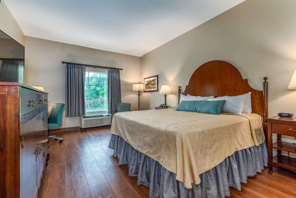 Bedroom with a large bed, wooden furniture, window, and desk. Cream and blue color scheme.