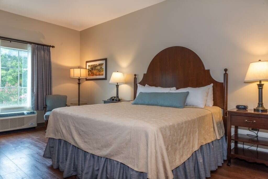 Bedroom with a king-sized bed, nightstands, a window, and a sitting chair; beige walls, dark wood floors.