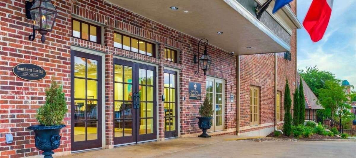 Exterior of a brick building with arched entrance, French doors, flags, and a landscaped area.