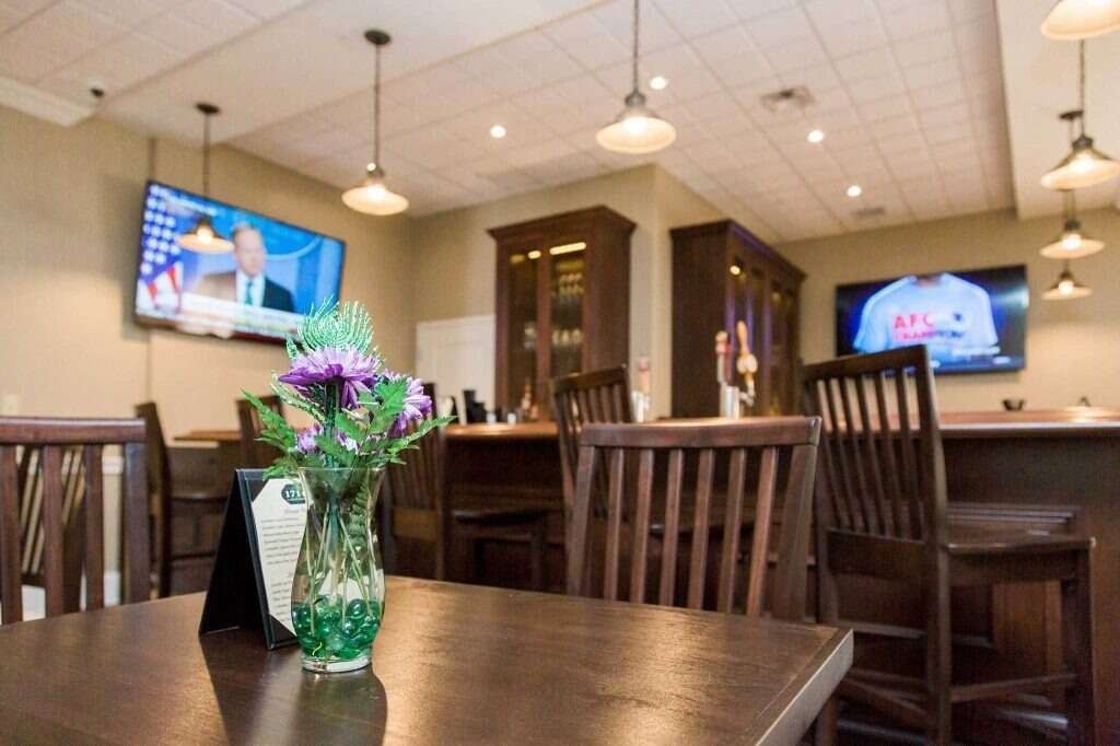 Bar with tables, chairs, dark wood bar, TVs, and hanging lights.