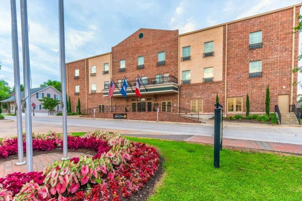 Hotel exterior with red brick, flags, and floral landscaping.