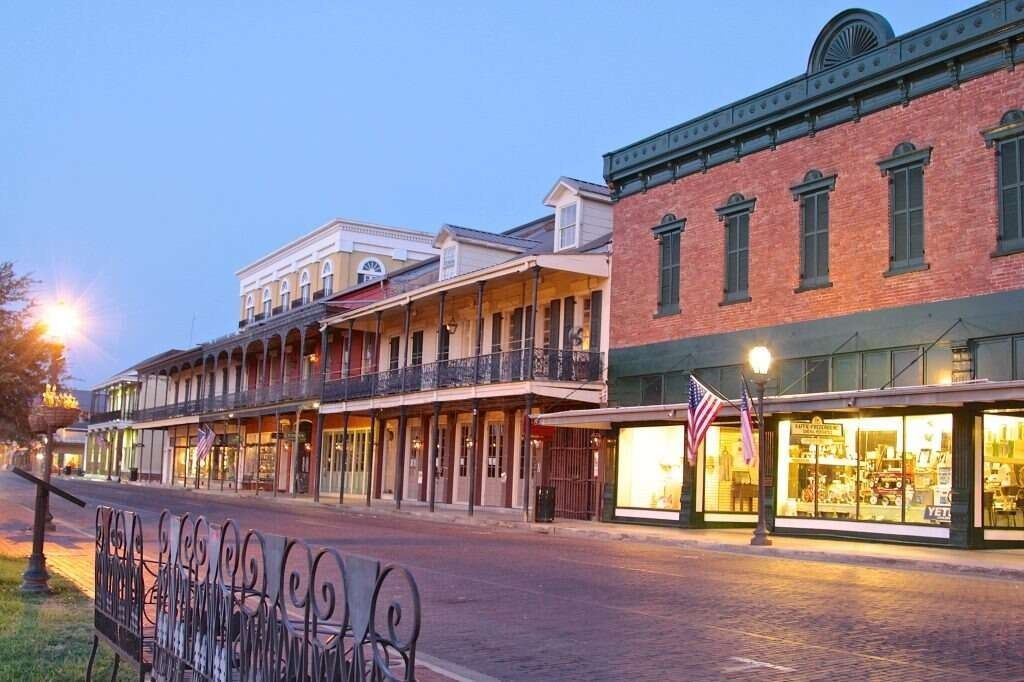 Historic street with buildings, awnings, and American flag. Dusk setting with lit shop windows.