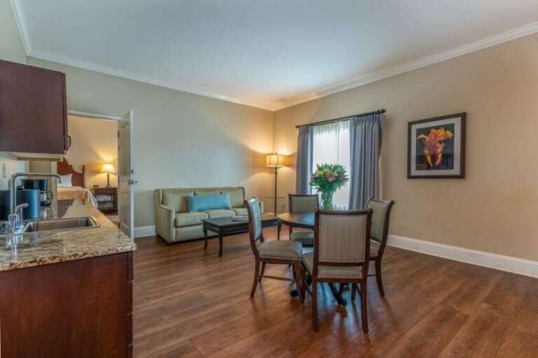 Spacious hotel suite with hardwood floors, seating area, dining table, and a view into the bedroom.